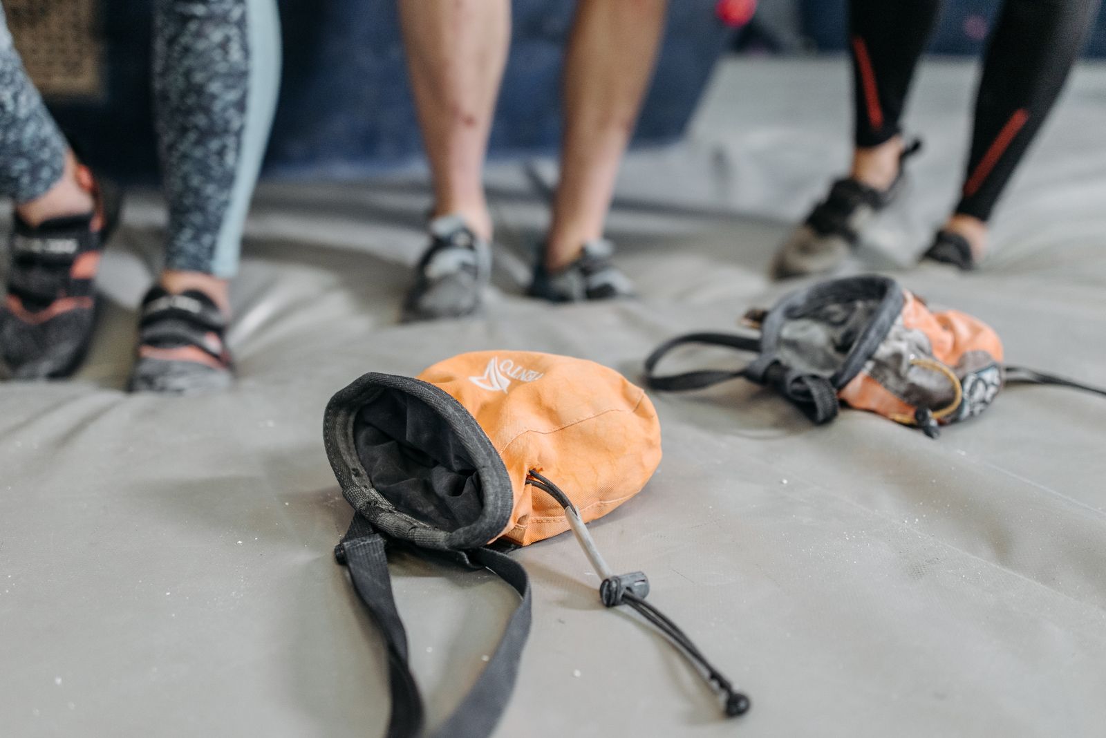 Chalk bags on a gym mat beside a pair of climbing shoes