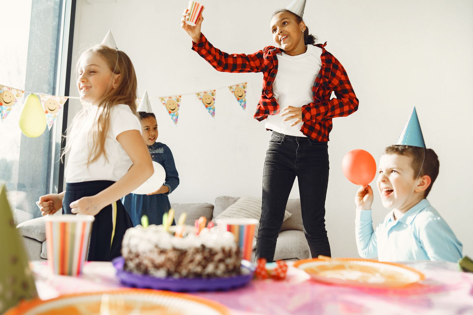 Children in party hats gathered around a birthday cake with candles