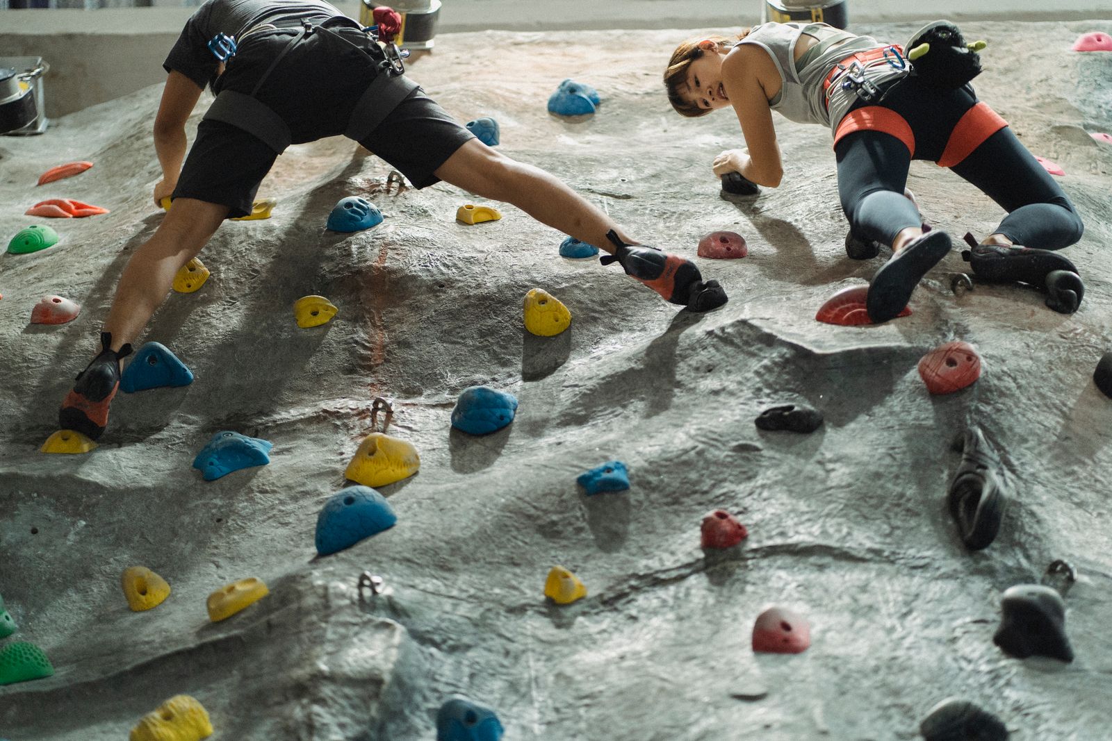 Two climbers stretching across a gray slab wall dotted with colorful holds