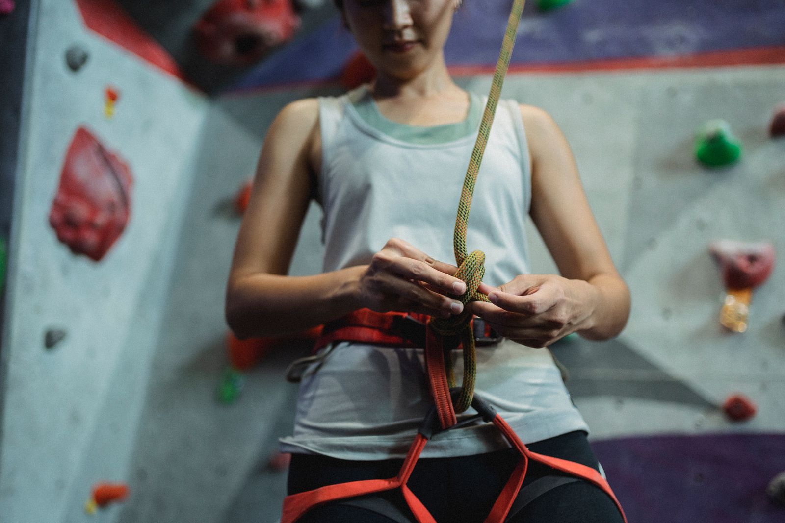 A climber in a harness tying in to a rope at the base of a rope wall