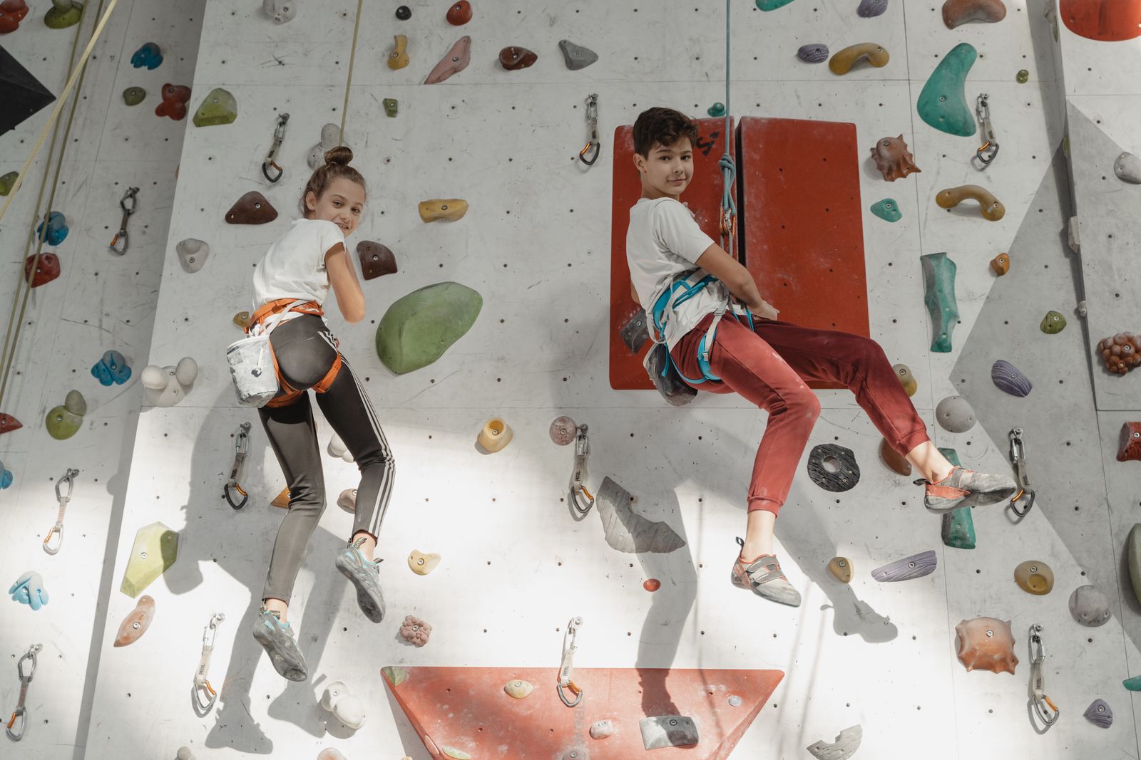 Two children in harnesses climbing a colorful rope wall